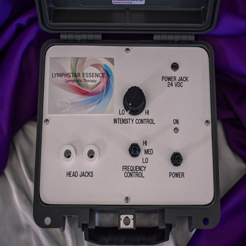 Lymphstar Essence Lymphatic Therapy device in a black carrying case, showing the front control panel with knobs, jacks, and a printed logo on a white background with purple fabric draped behind it.